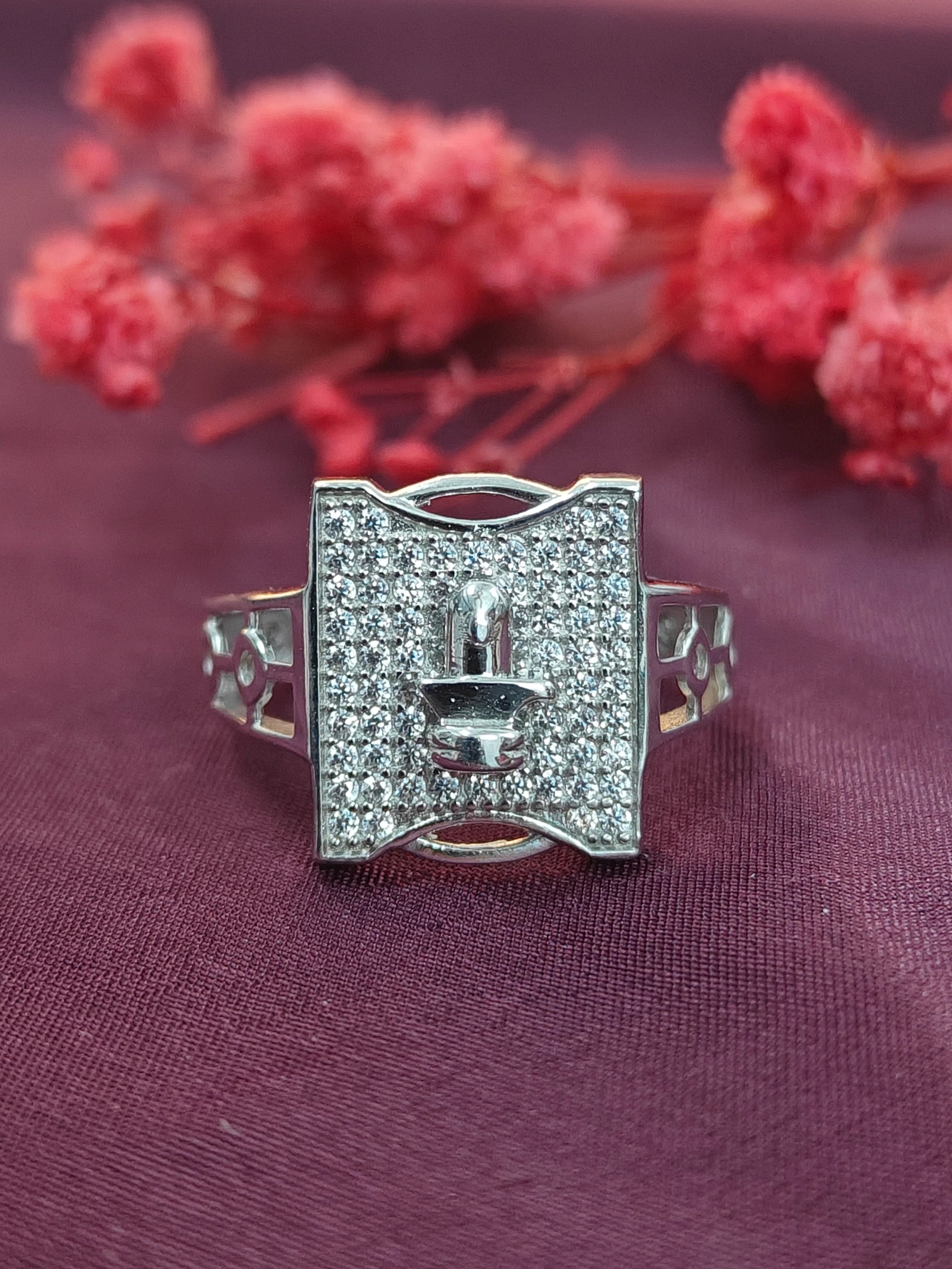 Silver ring with gemstones on a purple fabric background with red flowers.
